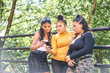 © Connect Images - Young woman with teenage sisters looking at smartphone in park