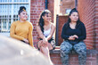 © Connect Images - Young woman and her teenage sisters sitting on wall looking away