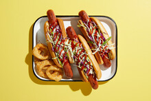 Three Hotdogs On Tray With Onion Rings, Overhead View On Yellow Background