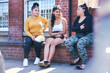 © Connect Images - Young woman and her teenage sisters sitting on wall talking