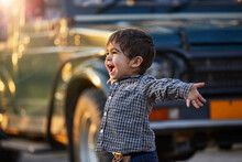 Excited Toddler With Open Arms Standing By A Large Vehicle