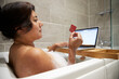 © Connect Images - Woman sitting in bathtub, having foam bath and shopping online on her laptop during Coronavirus crisis.