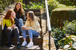 © Connect Images - Three teenage girls sitting outdoors on stairway, checking mobile phone.