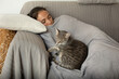© Connect Images - Woman and grey tabby cat sleeping on a sofa.