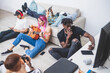 © Connect Images - Group of young men and women sitting on living room floor, checking their mobile phones, woman with long pink hair playing guitar.