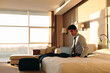 © Connect Images - Businessman using laptop on bed of hotel bedroom