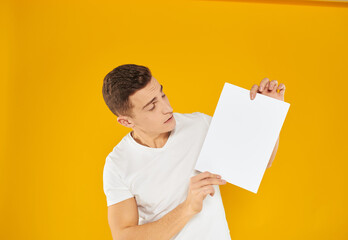 Guy with a white sheet of paper on a yellow background blank business card advertising