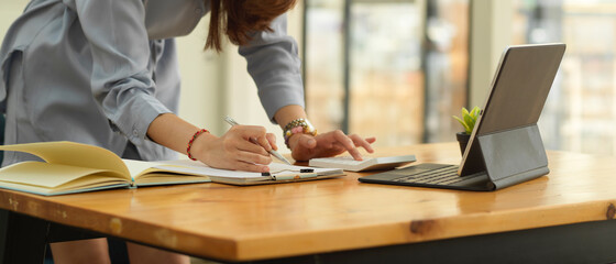 Female office worker standing working with paperwork and digital tablet at office desk