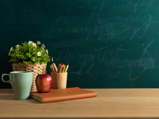 Wall Mural - Study table with notebook, apple, pencils and plant pot in classroom with blackboard background