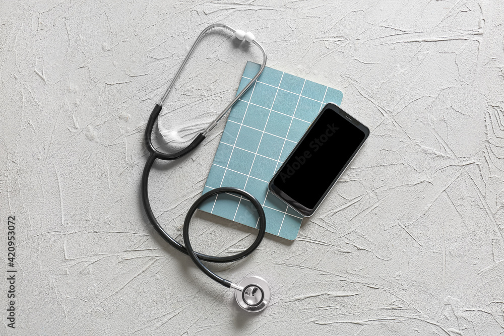 Modern stethoscope, notebook and mobile phone on grey background