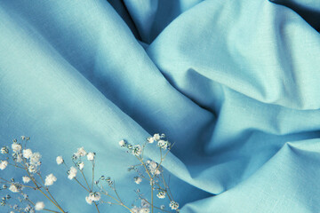 Draped beautiful folds of blue natural fabric background with shadows and white Gypsophila flowers. Close up