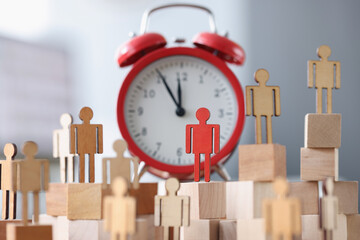 Wooden figurines with one red figure stand next to alarm clock