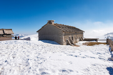 Typical old stone farmhouse and cow shed on Lessinia Plateau (Altopiano della Lessinia) in winter with snow near the peak of Corno d'Aquilio. Sant'Anna d'Alfaedo municipality, Veneto, Italy, Europe.