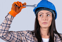Portrait Of A Young Woman Auto Mechanic In A Hard Hat And With A Key Looking To The Side On A White Background.