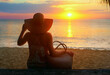 © soft_light - Vacation Summer Holiday Concept. Woman in dress with summer bag watching sunset on beach.