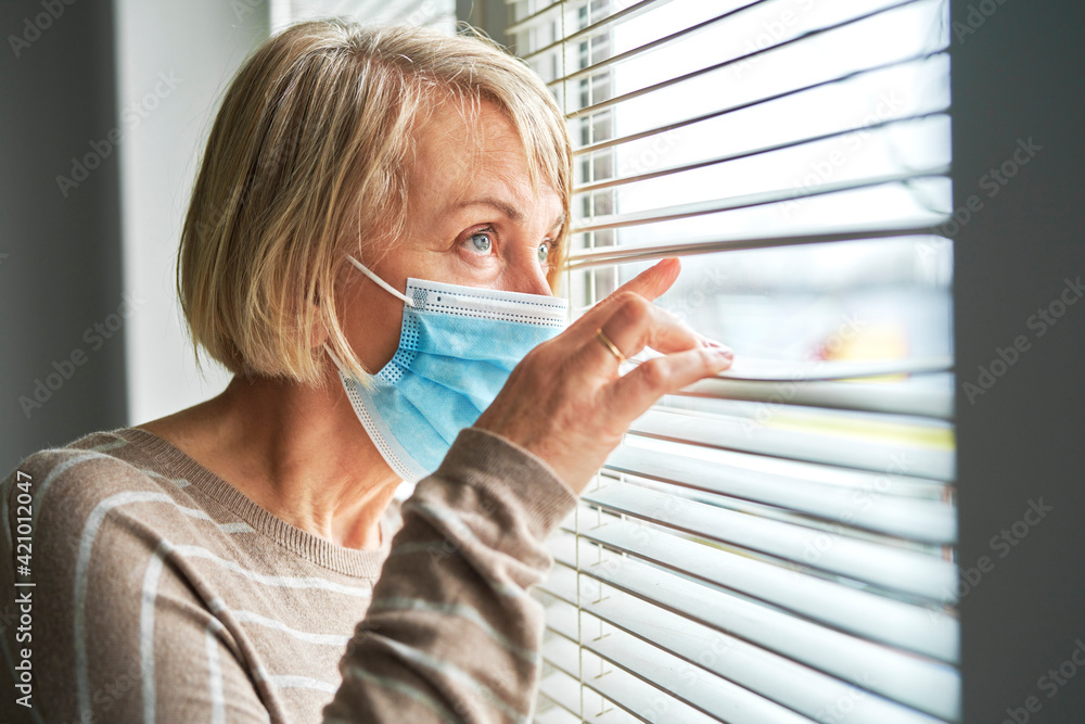 Quarantined senior woman wearing mask looks through blinds - obrazy, fototapety, plakaty 