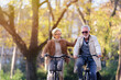 © lordn - Cheerful active senior couple with bicycle in public park together having fun. Perfect activities for elderly people. Happy mature couple riding bicycles in park