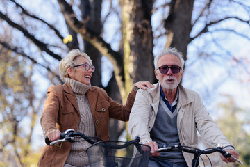 Wall Mural - Cheerful active senior couple with bicycle in public park together having fun. Perfect activities for elderly people. Happy mature couple riding bicycles in park