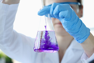 woman scientist dripping purple liquid into flask with solvent closeup