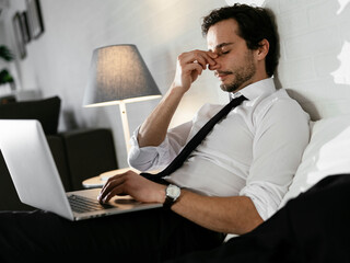 Young businessman rests after a long day. Man working on laptop in the bed.