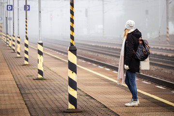 Female tourist with backpack waiting for train at empty railroad station platform. Woman travel by train