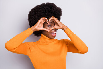 Poster - Photo of affectionate happy dark skin woman make heart shape fingers look eye isolated on grey color background