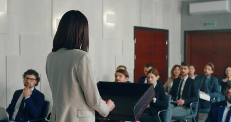 young stylish businesswoman standing behind podium speaking at conference and answers questions from