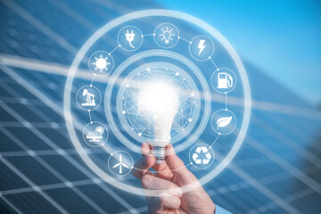 The man holds a light bulb, LED bulb on a background of solar panels with icons energy sources for renewable, sustainable development. Ecology concept.