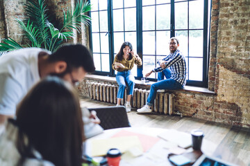 Wall Mural - Cheerful colleagues sitting on window sill in creative workplace