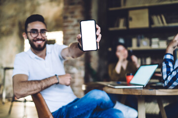 Wall Mural - Positive man demonstrating smartphone screen while cooperating with colleagues