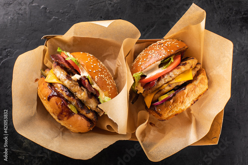 Two large grilled chicken burgers in a craft box on a dark background, top view. Takeaway hamburger. Burger in the box, fast food.