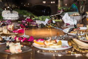 Wall Mural - Early morning after the party. Glasses and plates on the table with confetti and serpentine, leftovers, flower petals