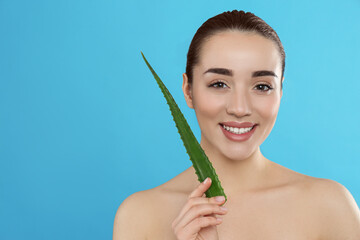 Young woman with aloe vera leaf on light blue background. Space for text