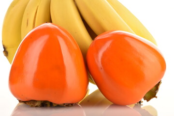 Two sweet juicy persimmons with a bunch of bananas, close-up isolated on white.