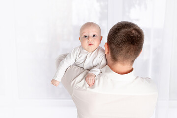 a father holds a newborn baby on his shoulder at home by the window, the concept of a happy loving family, father's day