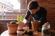 © Edgar - Hombre joven caucásico regando una planta encima de la mesa de la terraza de su casa. Cuidando plantas