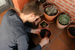© Edgar - Hombre joven caucásico sentado en el suelo de su terraza cuidando las plantes que tiene en las macetas. Añadiendo tierra para las plantas