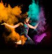 Expressive young woman makes a high jump with explosion of dry colorful holi powder. Holi colour splash