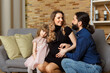 © BY-_-BY - Happy young father, mother and daughter sit on wicker sofa at home.