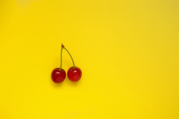 Two red cherries on a yellow background, top view, natural product. Horizontal format. Advertising model.Place for text