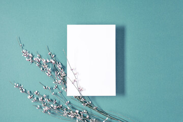 White paper empty blank, flowers on blue background. Invitation card mockup on white table. Flat lay, top view, copy space, mock up