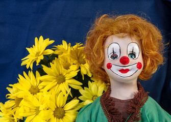 antique clown doll with orange hair and yellow daisies on blue background