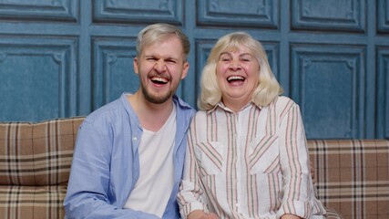 Happy senior older mother and smiling young adult grown son hugging laughing looking at camera