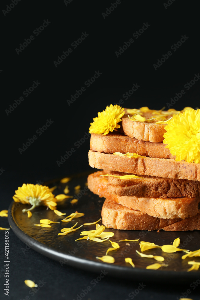 Plate with fresh toasts and flowers on dark background