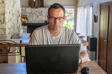 A man working at home, using a laptop computer, using internet, reading news, doing online shopping order for delivery, or studying with device online.