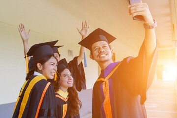 Wall Mural - The university graduates in graduation gown and a mortarboard cap with a degree certificate in hand celebrating education achievement in the commencement ceremony. Congratulations to the graduations