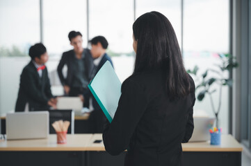 Wall Mural - Confident and smart beautiful businesswoman in formal attire stands in the office. With a group of friends and laptop in the background. A cheerful idea to work within the workspace.