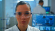 © DC Studio - Close up of tired scientist doctor looking at camera smiling working in equipped lab. Chemist examining virus evolution using high tech and chemistry tools for scientific research, vaccine development