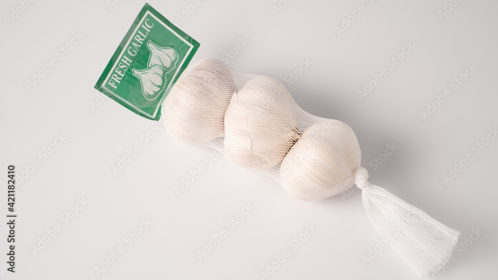 Garlic in net. Garlic packaging nets. Three garlic heads packaged in a mesh bag. Fresh garlic head wrapped in mesh bag Stock Photo Adobe Stock