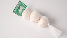 Garlic In Net. Garlic Packaging Nets. Three Garlic Heads Packaged In A Mesh Bag. Fresh Garlic Head Wrapped In Mesh Bag